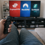 Person holding Amazon Firestick remote watching ExpressVPN, NordVPN and Surfshark logos on TV – Best VPN for Firestick Canada guide